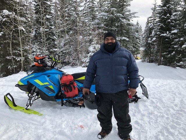 A man standing in the snow next to his snowmobile.