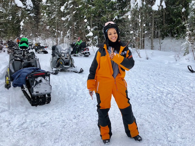 A woman in orange and black snowsuit standing on snow covered ground.