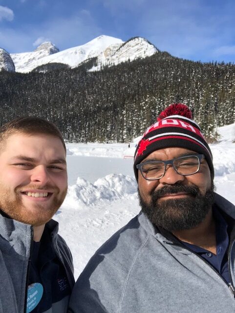 Two men standing in the snow with a mountain behind them.