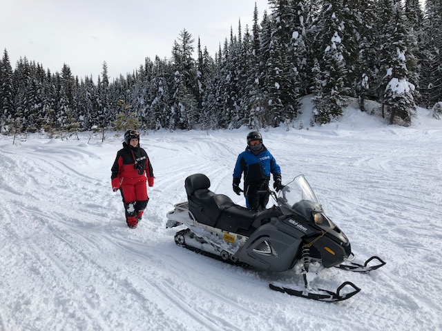 Two people on a snow mobile in the snow.