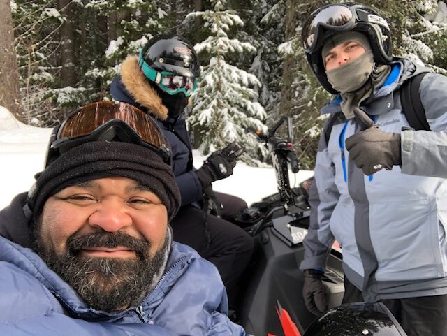 A man and two men on motorcycles in the snow.