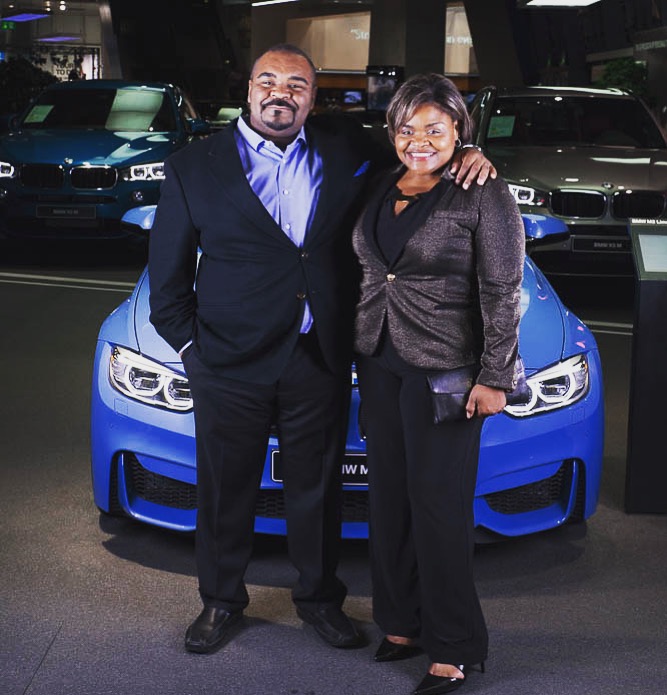 A man and woman standing in front of a blue car.