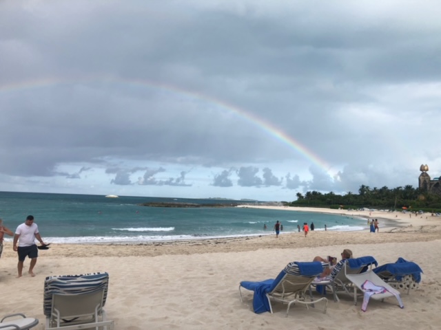 A rainbow over the ocean and people on the beach.