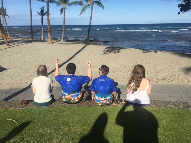 Four people sitting on the grass near a beach.