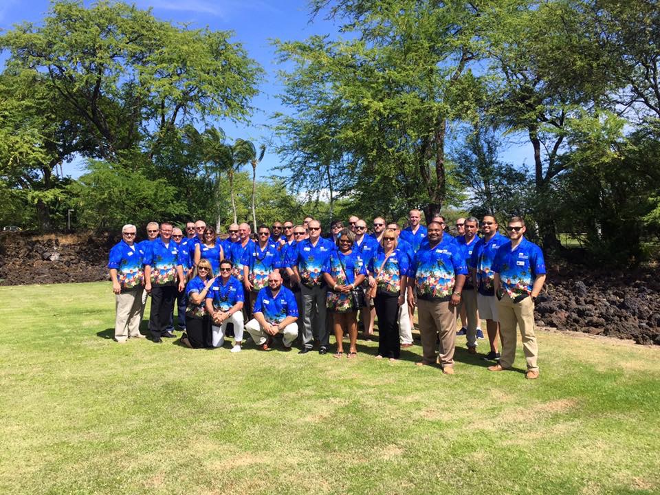 A group of people in blue shirts standing on top of a grass covered field.